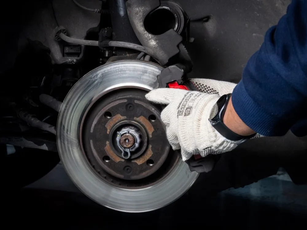 Gloved hands servicing an exposed brake rotor and caliper