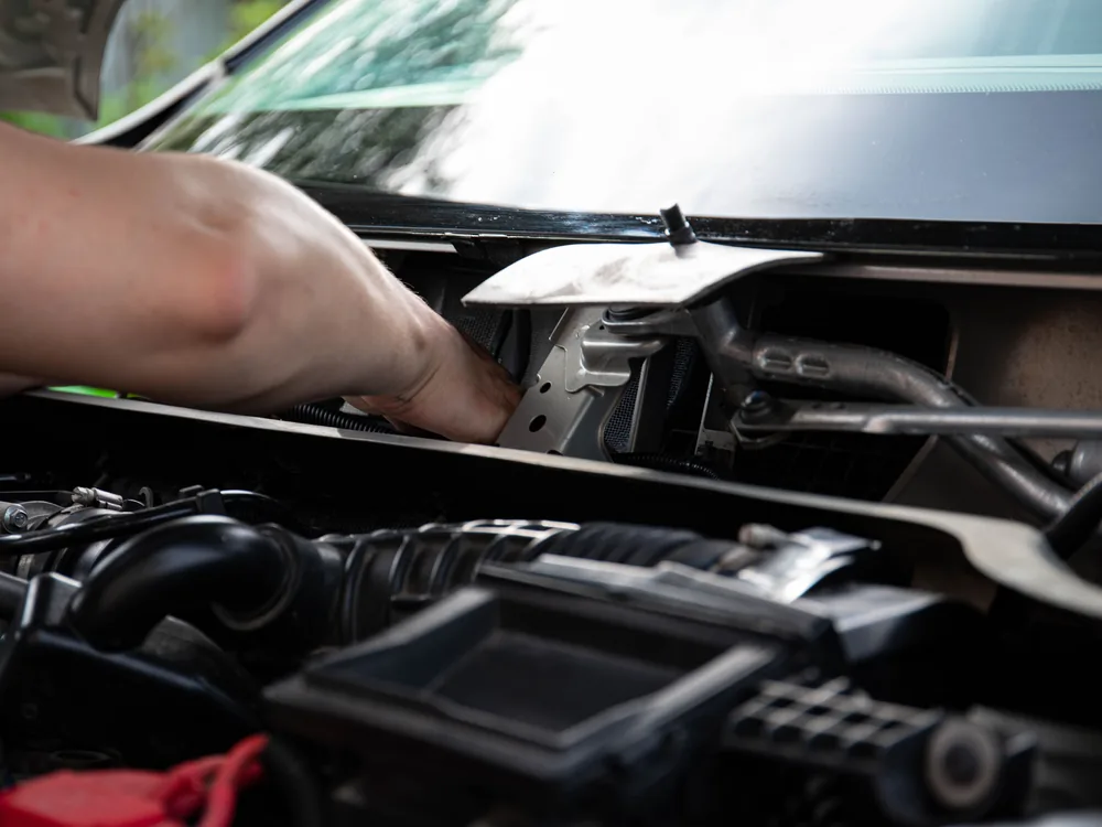 Hands working among components under an open car hood
