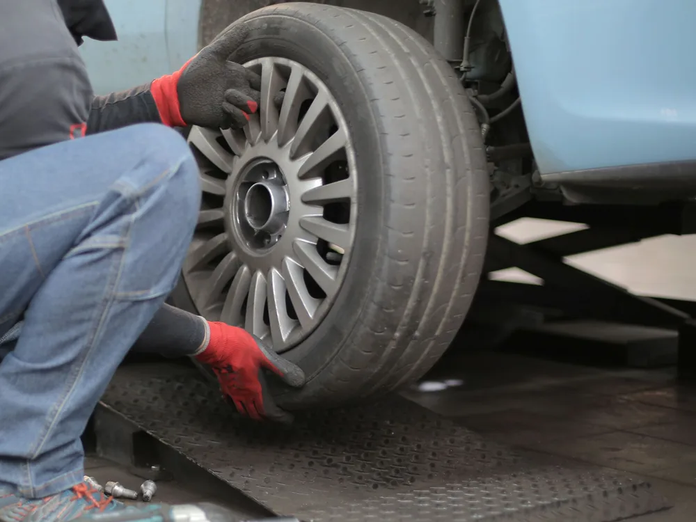 Gloved hands positioning a wheel on a raised car